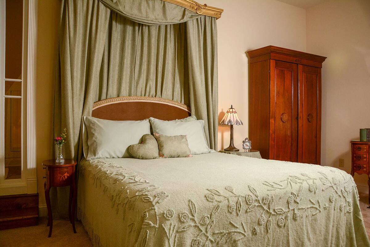 A bedroom with a canopy bed, a nightstand with a lamp, and a wooden wardrobe.