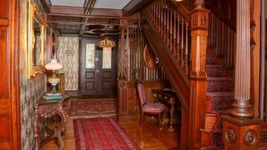 A grand staircase with ornate woodwork and a red carpet leading to a door. - The Towers Bed & Breakfast (Milford)
