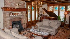 A spacious living room with a fireplace, a grand piano, and a chandelier. - The Towers Bed & Breakfast (Milford)