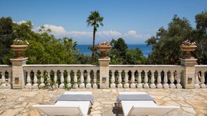 A terrace with two white lounge chairs, a stone balustrade, and a view of the sea.