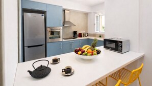 A compact kitchen with a refrigerator, oven, microwave, and a bowl of fruit on the counter.