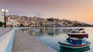 A waterfront scene with boats docked, a promenade, and buildings in the background. - Agrilos House - Amazing sea view - Sleeps 4 (Mirsini)