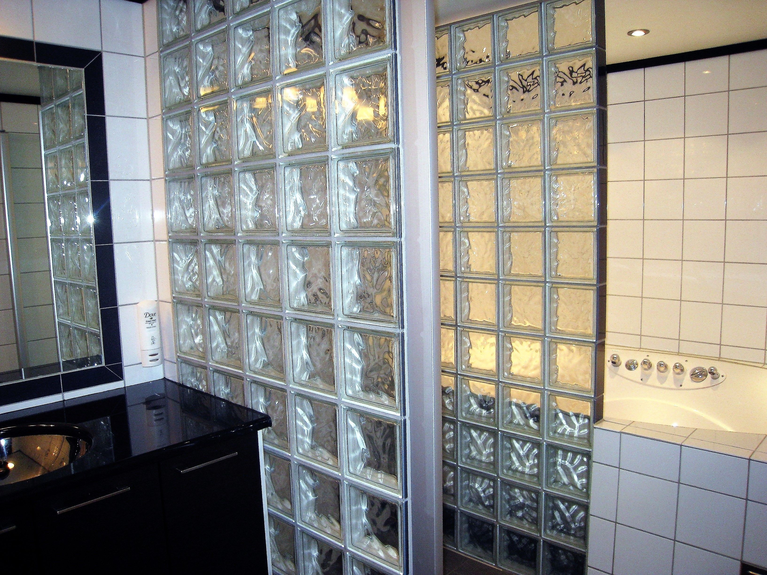 Een badkamer met een glazen scheidingswand, een zwart aanrecht en een witte betegelde muur met een bad.