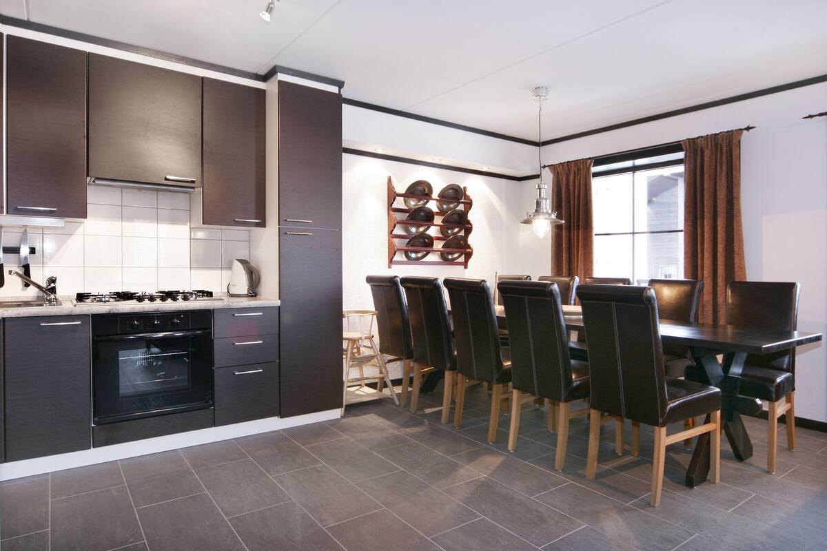 Una cocina moderna con armarios oscuros, horno empotrado y comedor con mesa y sillas de madera.