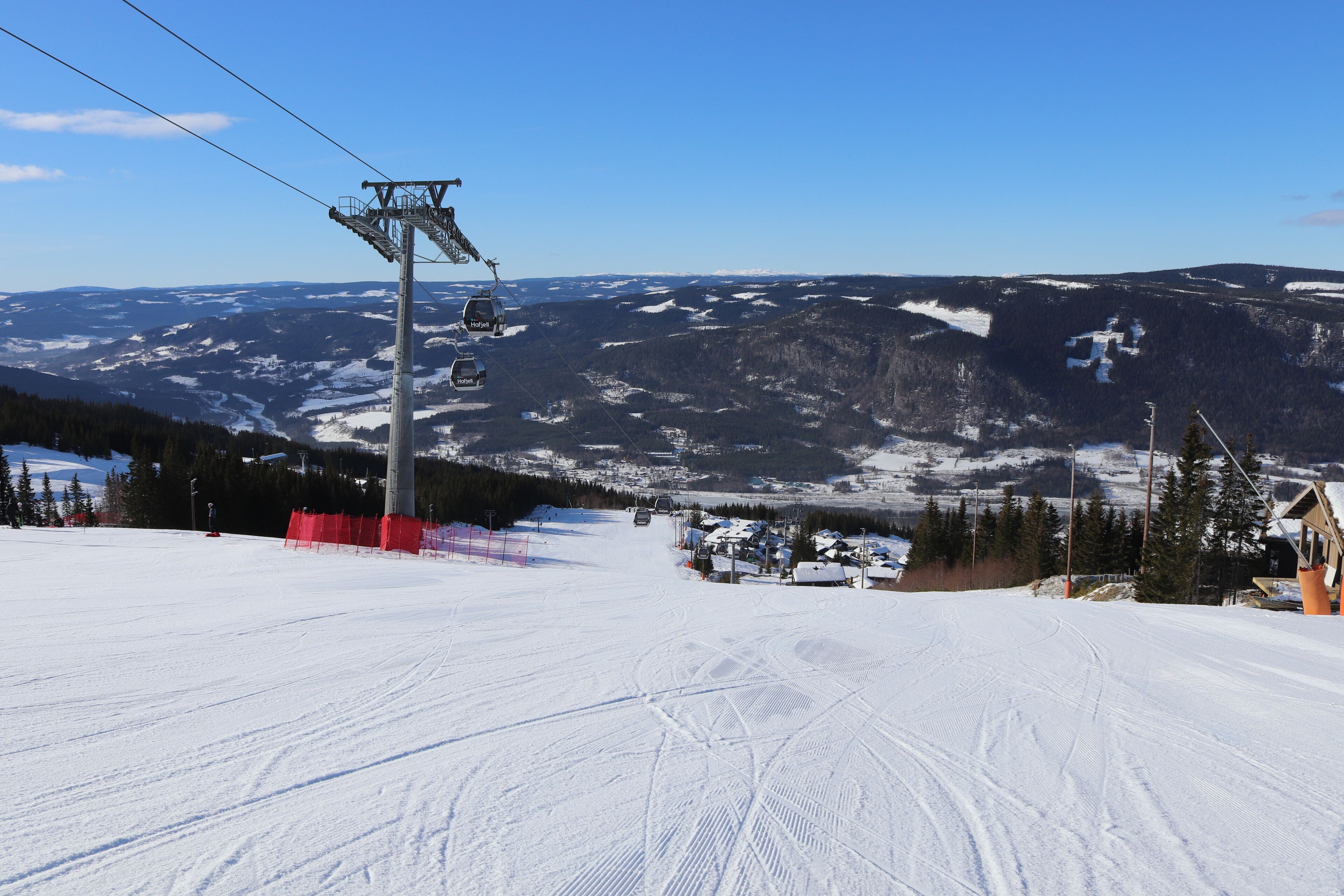 Pista de esqui com teleférico, montanhas cobertas de neve e céu claro.