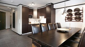 Una cocina moderna con armarios oscuros, un comedor con una mesa larga y sillas, y un escurreplatos montado en la pared.