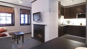 Una sala de estar moderna con chimenea, un televisor montado en la pared y una cocina con armarios oscuros y estufa.