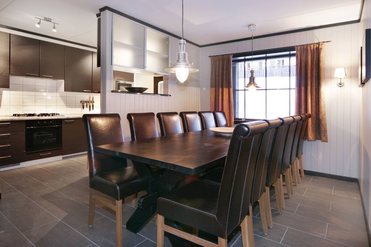 Una cocina moderna con armarios oscuros, una mesa de comedor grande con sillas de cuero y una ventana con cortinas.