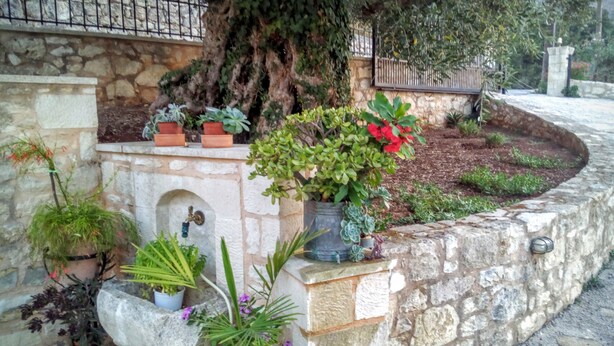 A stone wall with potted plants and a water feature. - TZITZIFES OLD STONE MANSION (Χανιά)