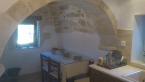 A kitchen with an arched stone wall, a window, and basic furnishings including a table, chairs, and a coffee maker. - TZITZIFES OLD STONE MANSION (Χανιά)