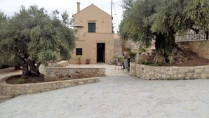 A stone courtyard with a building featuring a small entrance and a staircase leading to a second floor. - TZITZIFES OLD STONE MANSION (Χανιά)