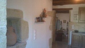 A rustic kitchen with stone walls, a shelf with pottery, and wooden cabinets. - TZITZIFES OLD STONE MANSION (Χανιά)
