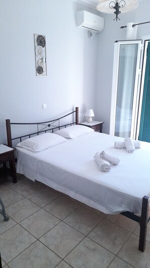 A neatly made bed with white linens, a bedside lamp, and a wall-mounted air conditioner.
