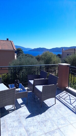 Eine Terrasse mit Korbmöbeln und Blick auf das Meer und die Berge.