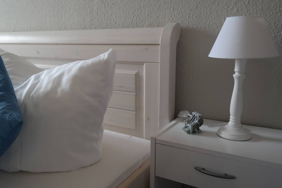 A bed with white and blue pillows, a white bedside table with a lamp, and a small decorative item.