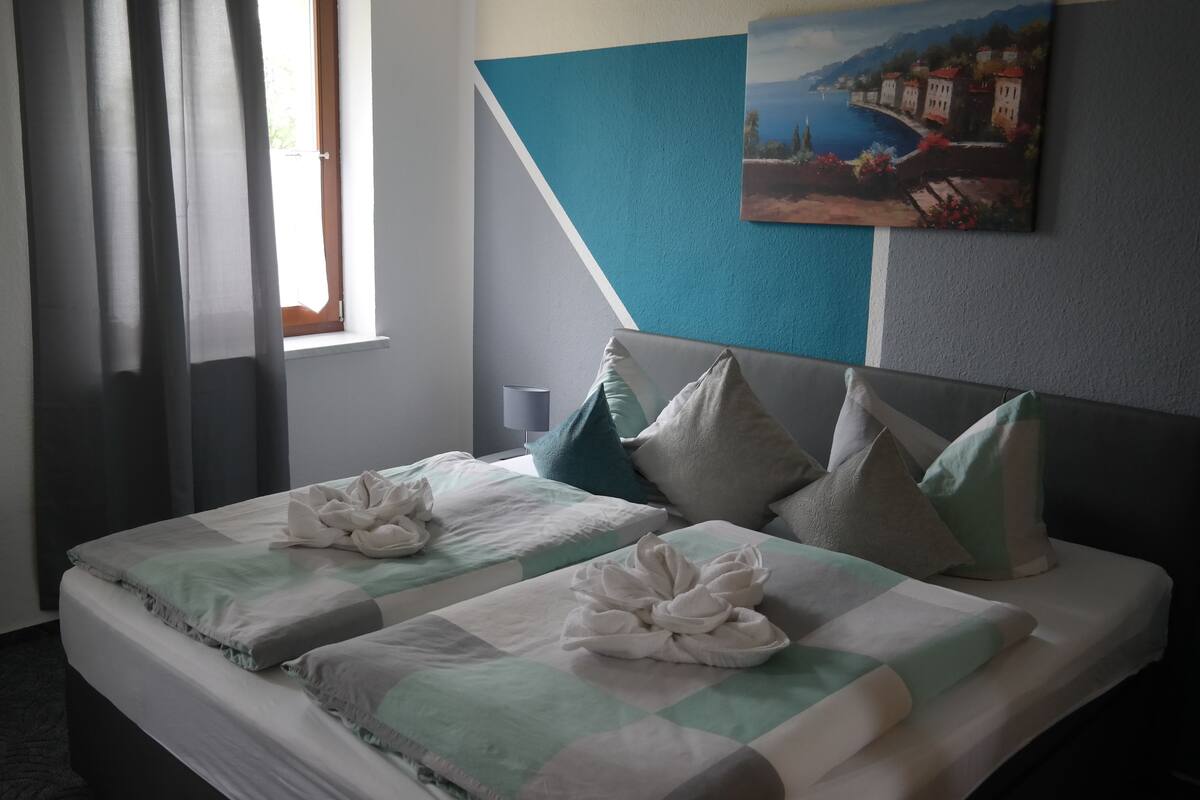 A hotel room with two beds, a painting on the wall, and a window with curtains.