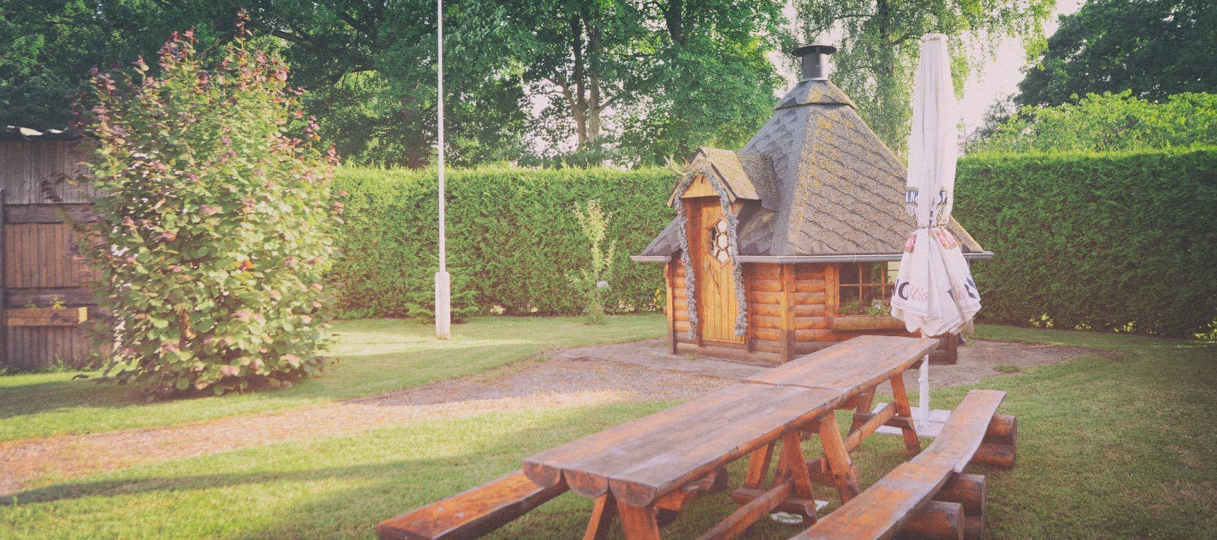 Ein Holztisch mit Picknickplatz und eine kleine Holzhütte mit Schornstein, umgeben von einer gepflegten Rasenfläche und einem Holzzaun.