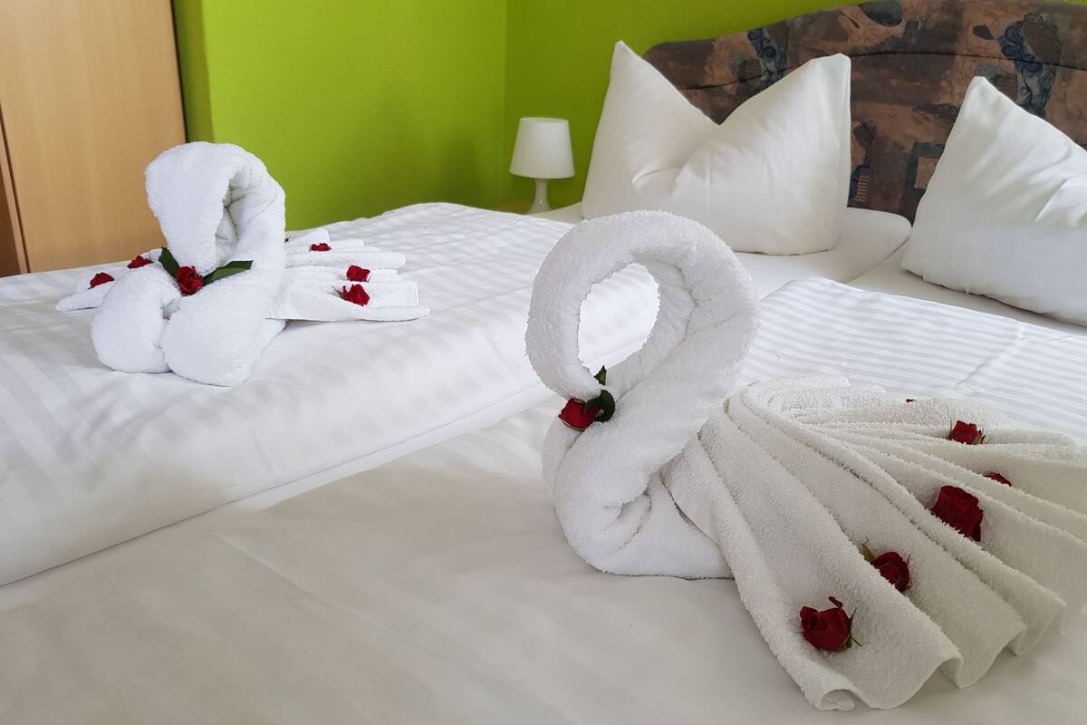 A hotel room with a neatly made bed, white towels, and rose petals.
