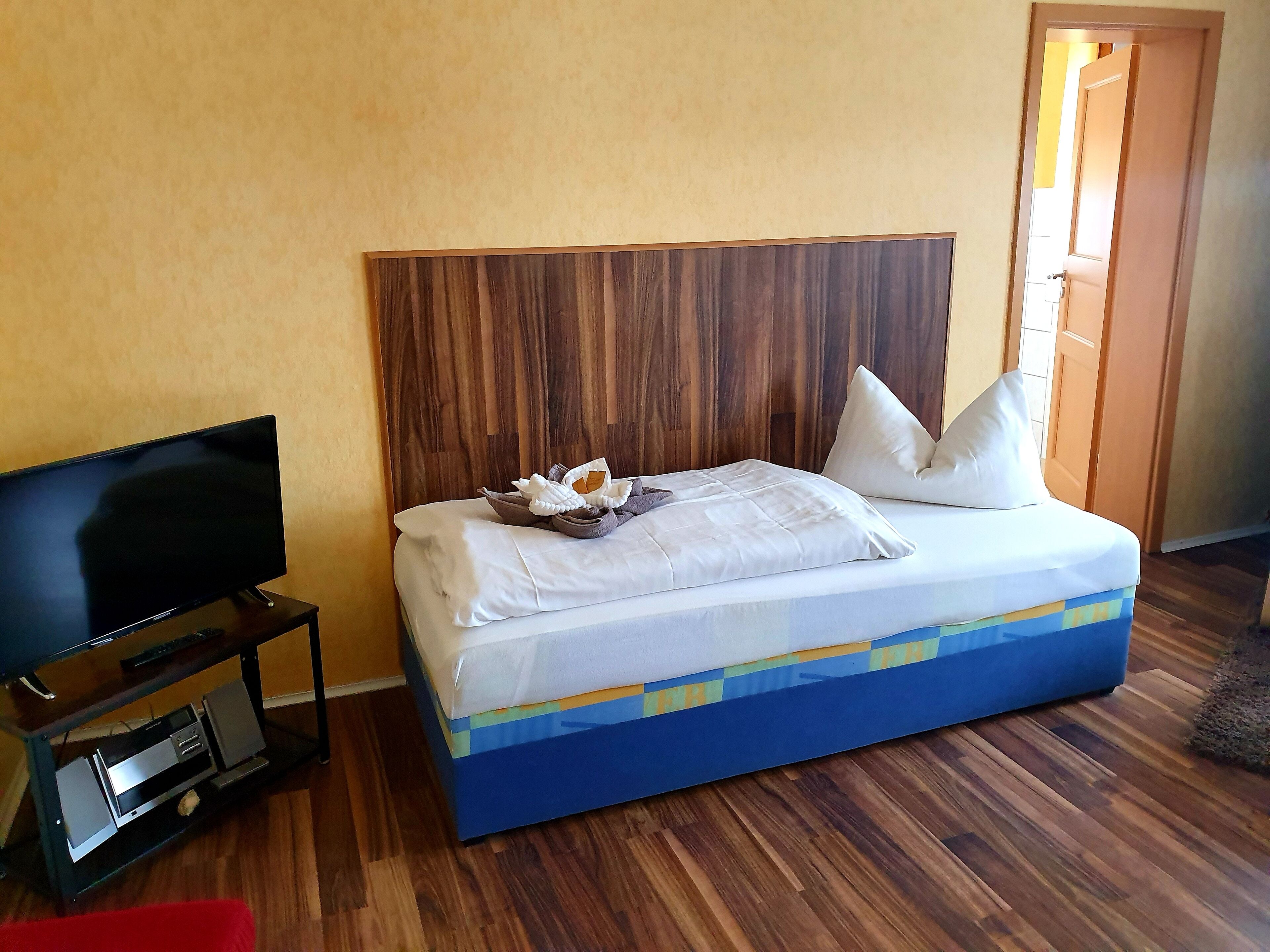 A hotel room with a bed, a television on a stand, and a wooden headboard.
