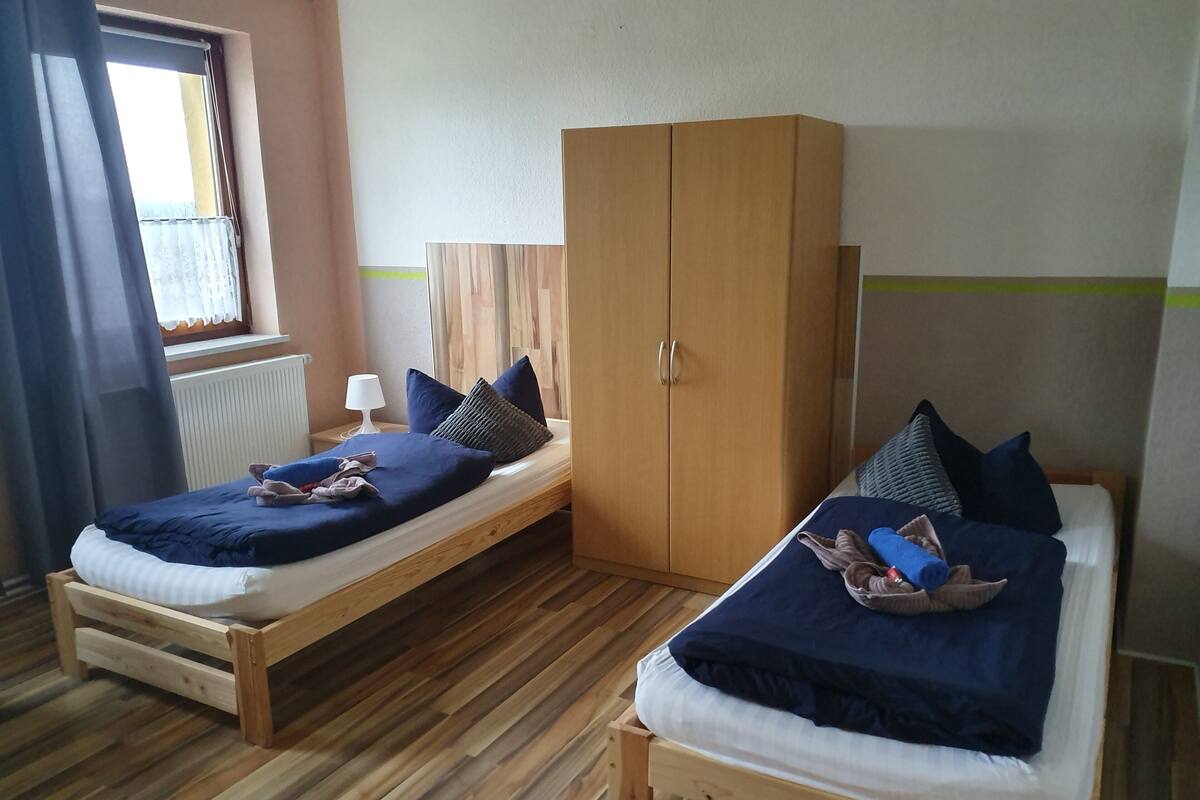 A room with two wooden beds, a wardrobe, a window with curtains, and a radiator.
