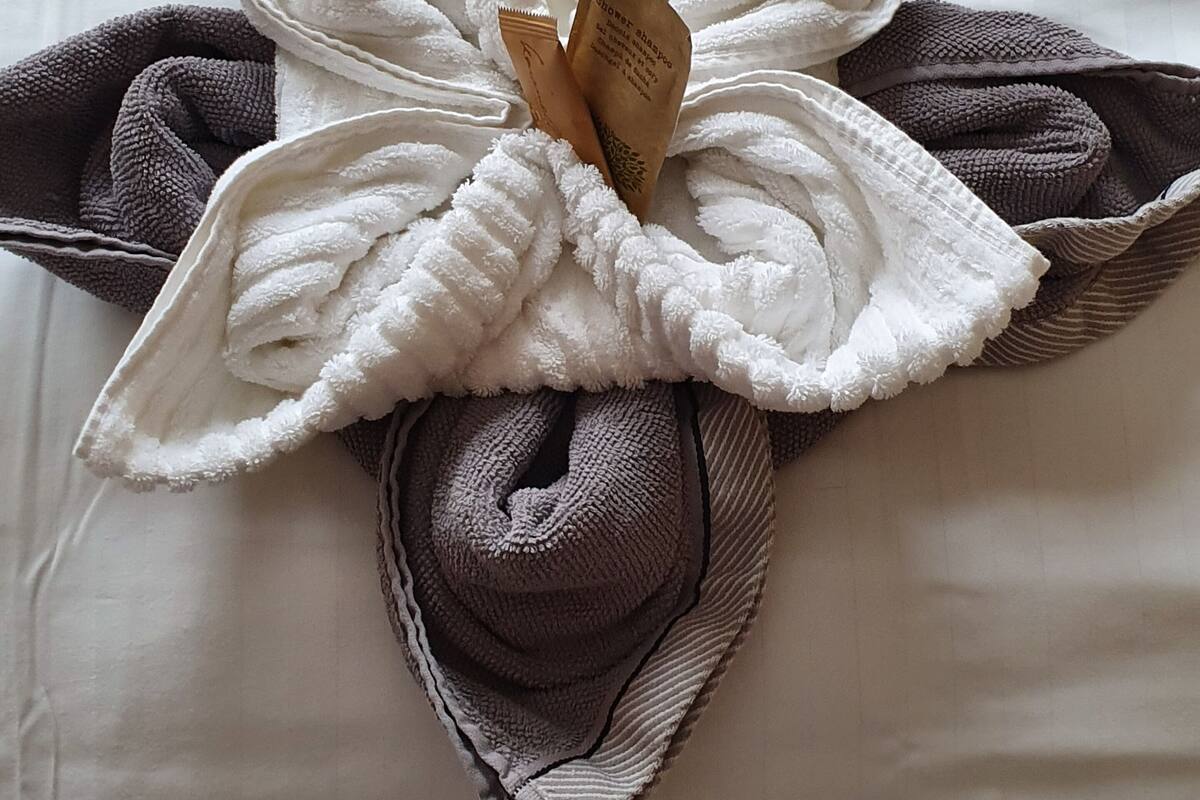 A neatly folded towel with a shower bottle attached, placed on a bed with white sheets.