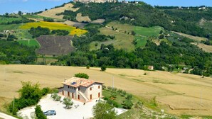 A rural house with a stone exterior, surrounded by fields and a hill in the background.