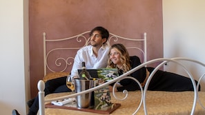 A bed with a metal frame, a bottle of wine, and a glass on a tray. - Agriturismo Oasi Biologica (Montedinove)