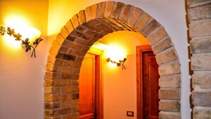 A hallway with a brick archway, wooden doors, and wall-mounted light fixtures.