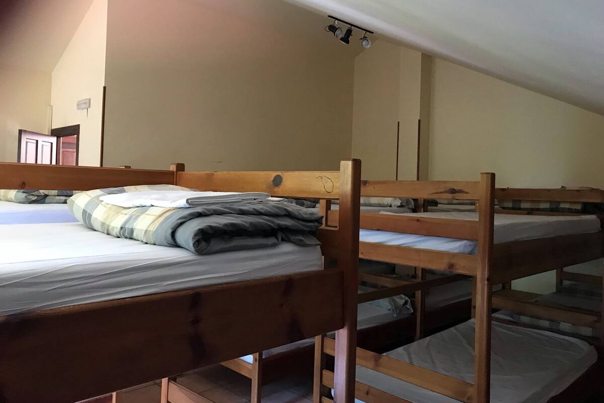 Une chambre de dortoir avec des lits superposés, un luminaire au plafond et une porte visible au fond.