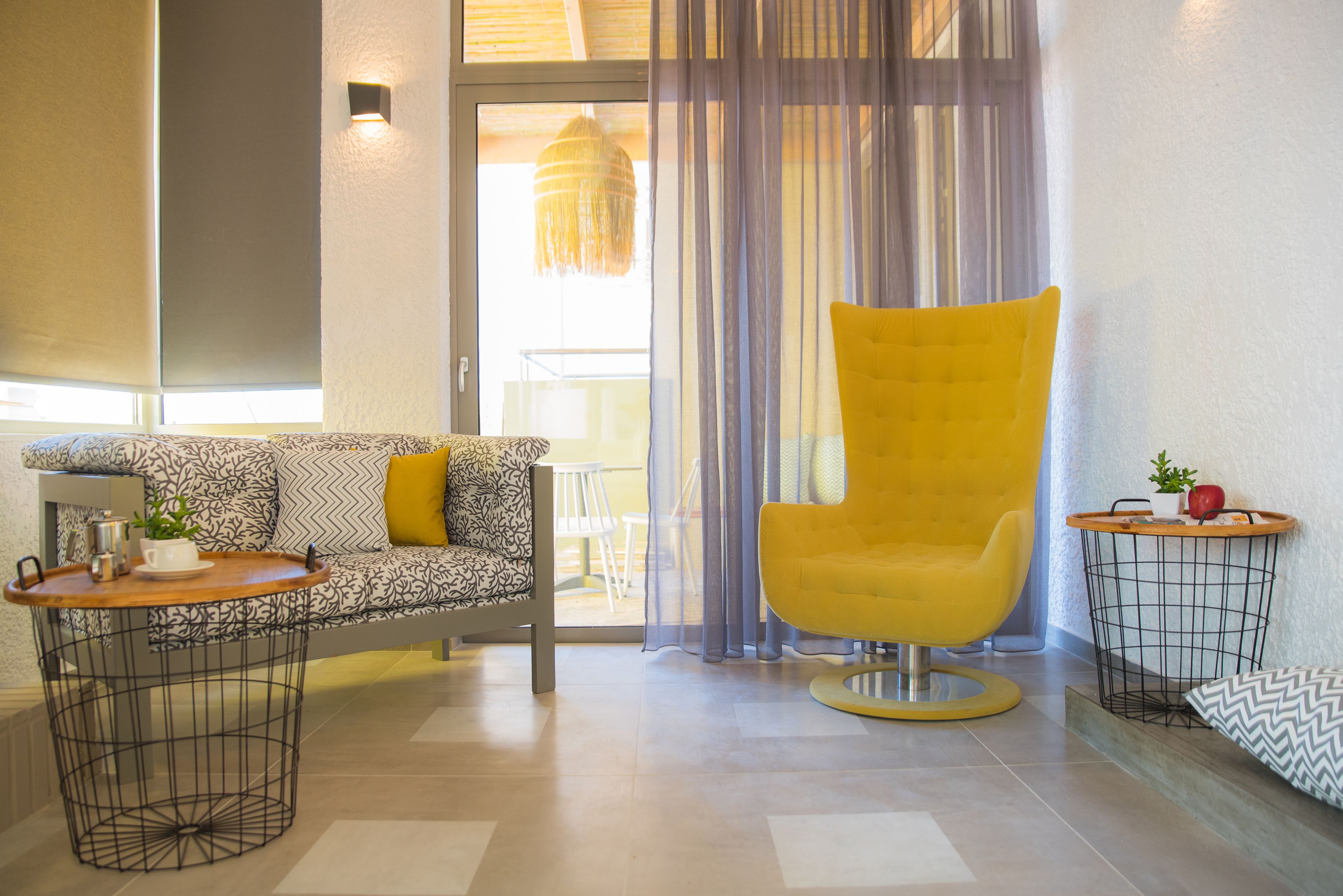 A modern living room with a patterned sofa, a yellow armchair, a small round table with a tray, and a side table with a plant.