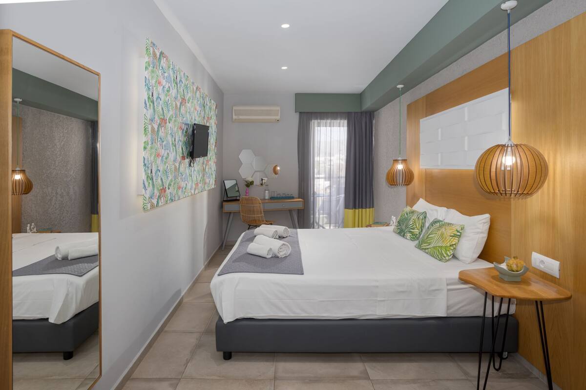 A modern hotel room with a large bed, a desk, a chair, a TV, and a mirror.