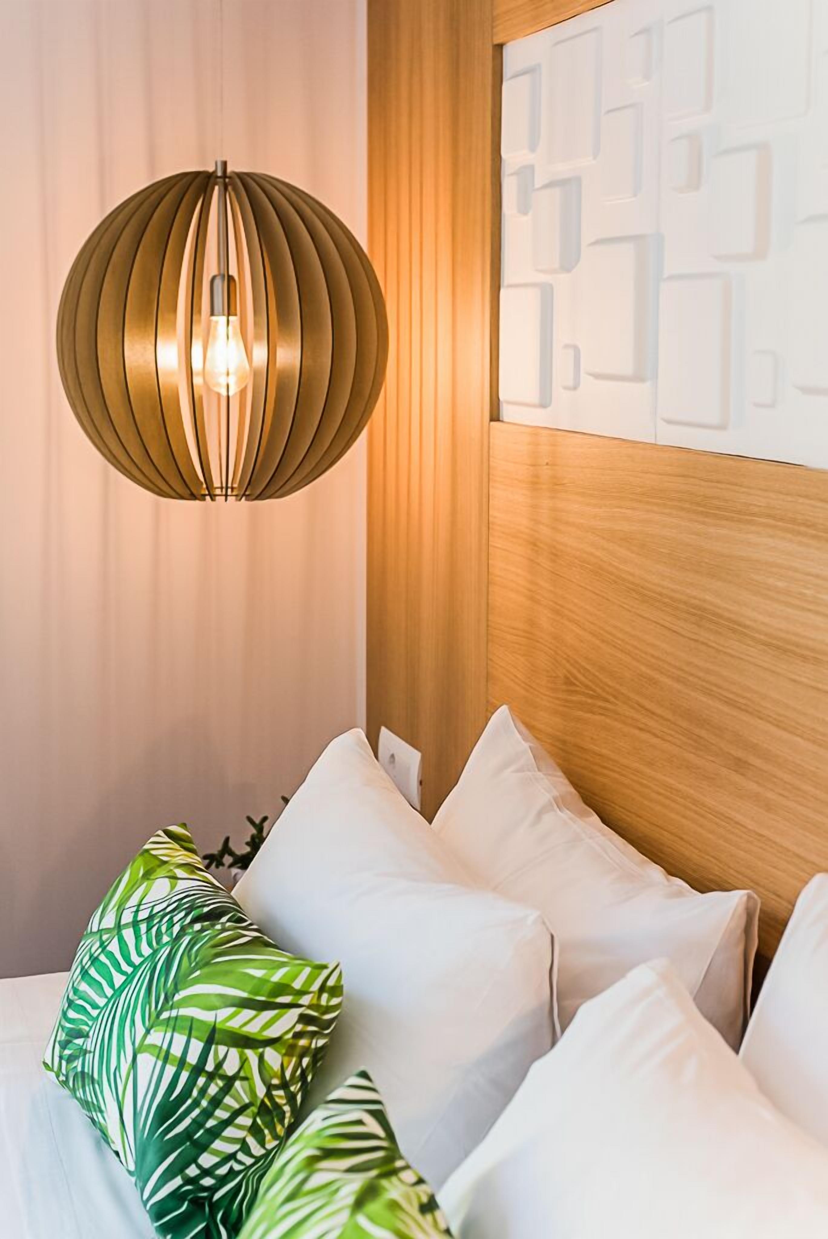 Ein modernes Schlafzimmer mit einem hölzernen Kopfteil, einer hängenden Pendelleuchte und einem Bett mit weißen und grünen Kissen.