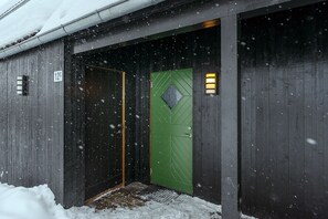 A wooden building with a green door, a number '12' sign, and a small entrance area with a doormat.