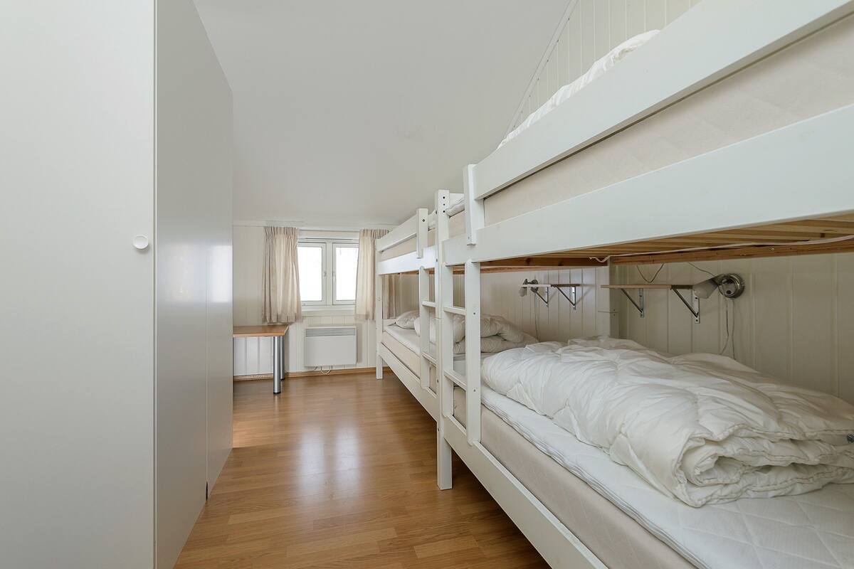 A bunk bed room with a wooden floor, a window with curtains, and a radiator.