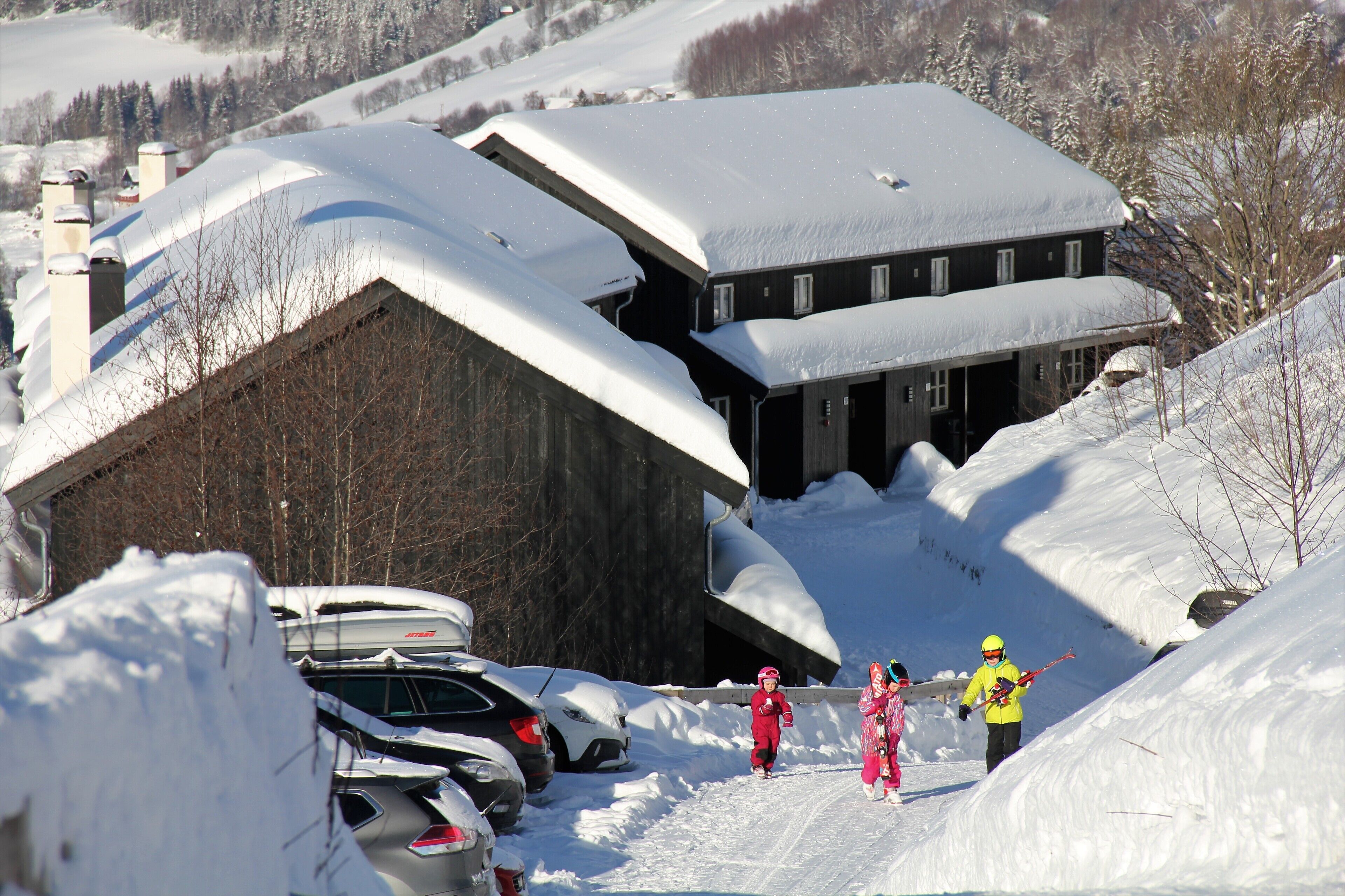 Um edifício coberto de neve com telhado inclinado, carros estacionados e paisagem nevada.