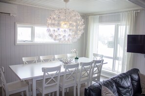 A dining area with a white table and chairs, a decorative hanging light, and a television mounted on the wall. - Hafjell Resort Hafjelltoppen Gaiastova (Øyer)