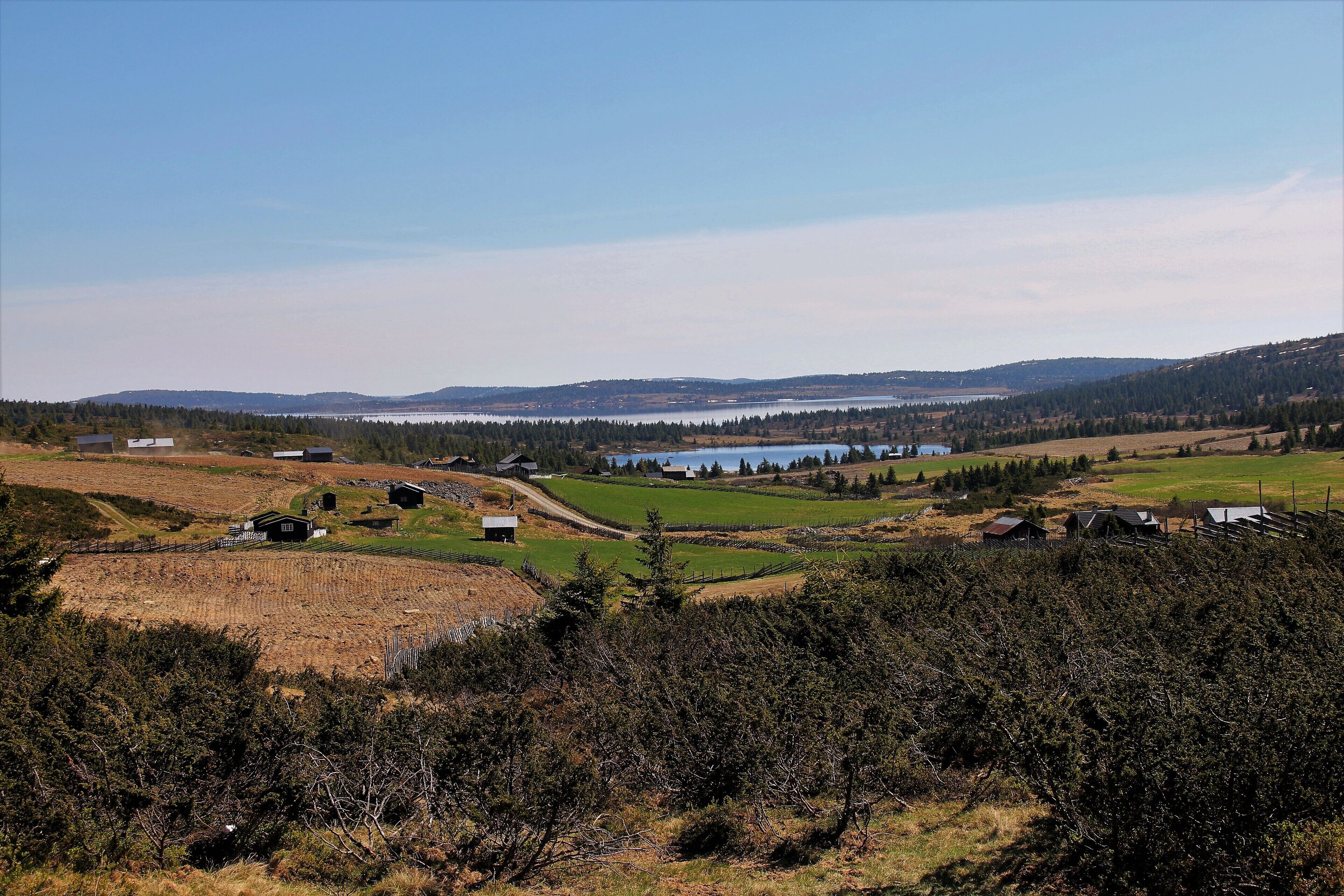 Een landelijk landschap met velden, een meer en verspreide gebouwen.
