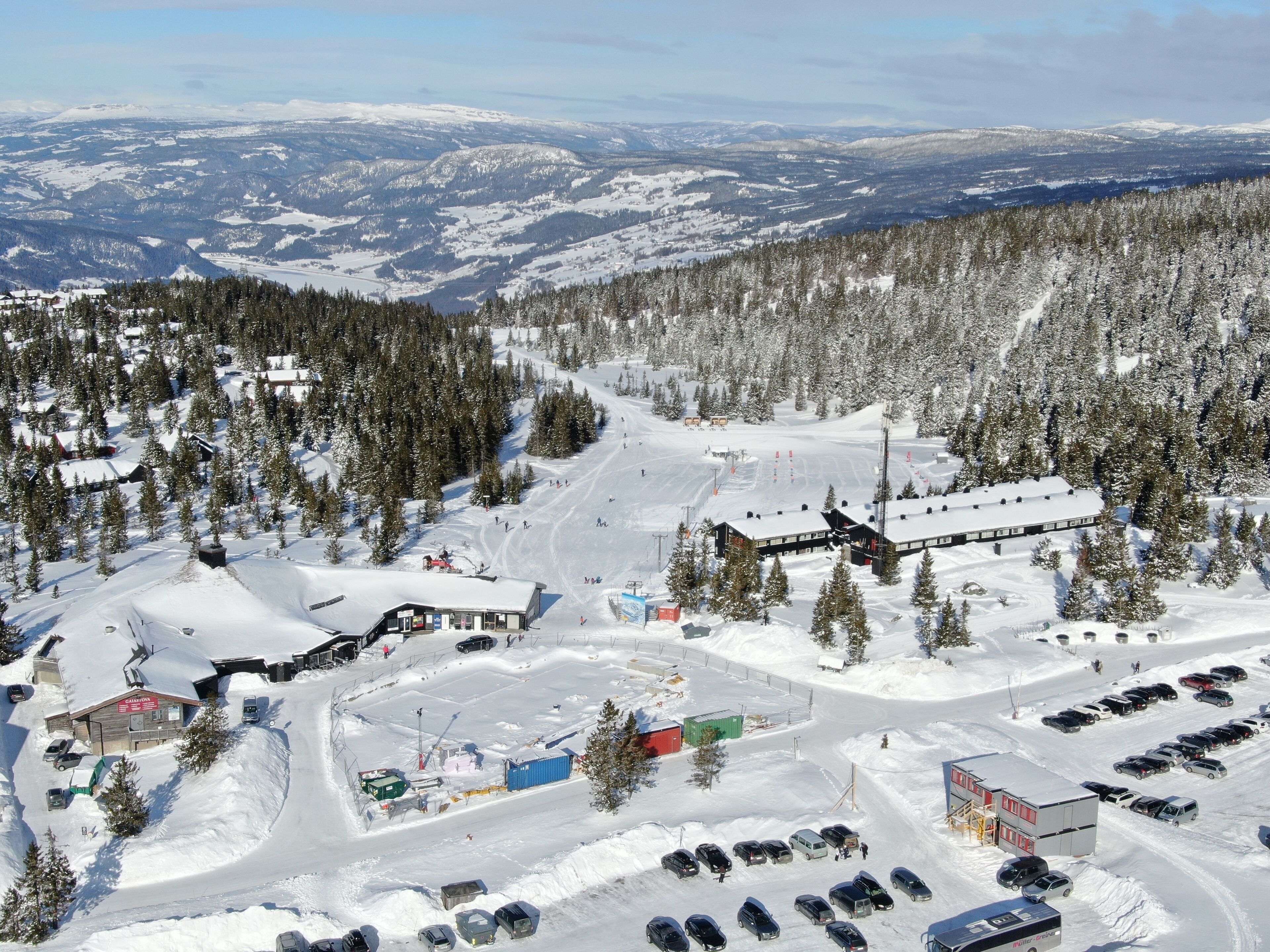 Estación de esquí nevada con parqueadero, edificios y montañas al fondo.