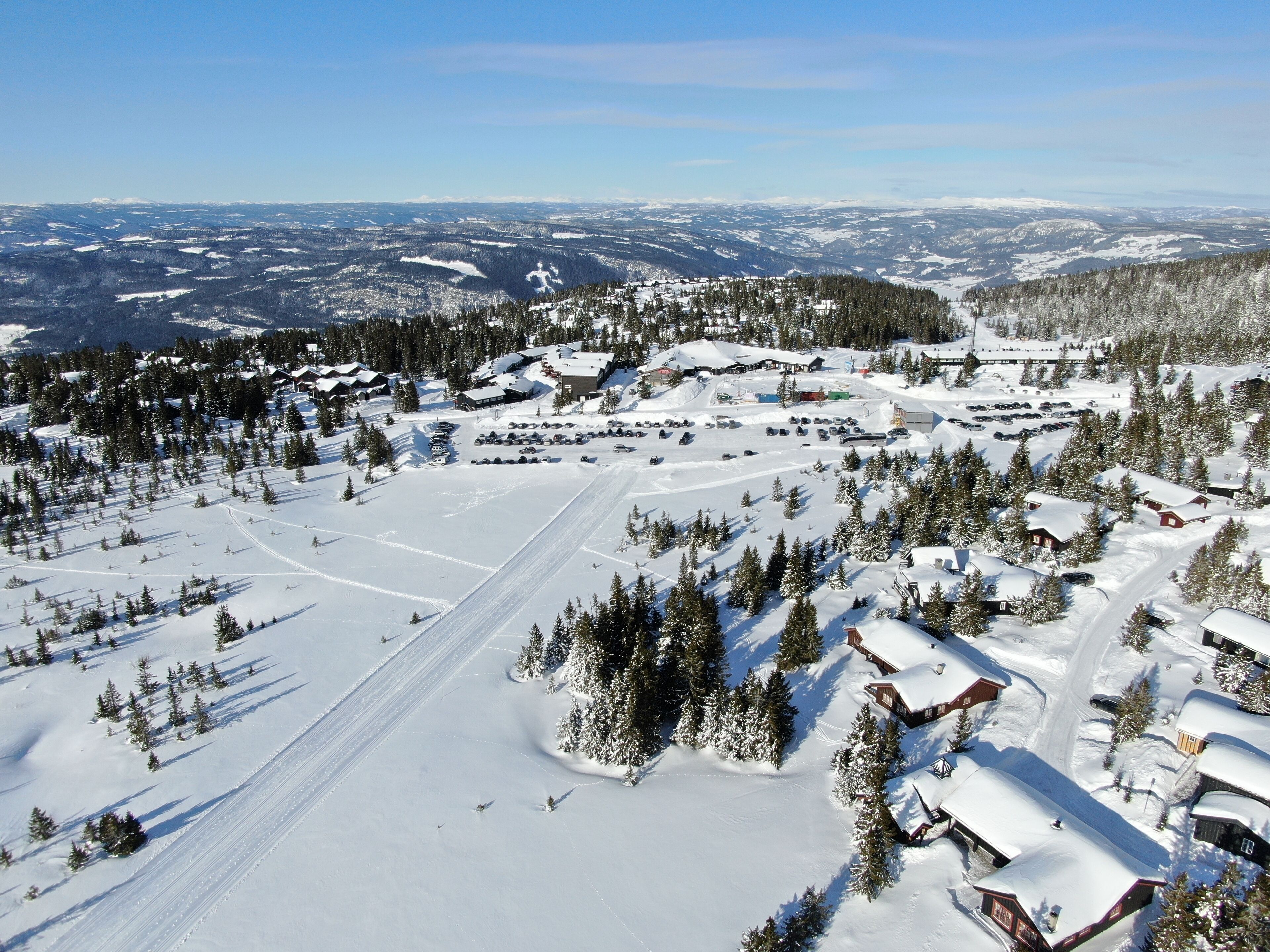 A snow-covered ski resort with multiple buildings, ski trails, and a vast mountain backdrop.