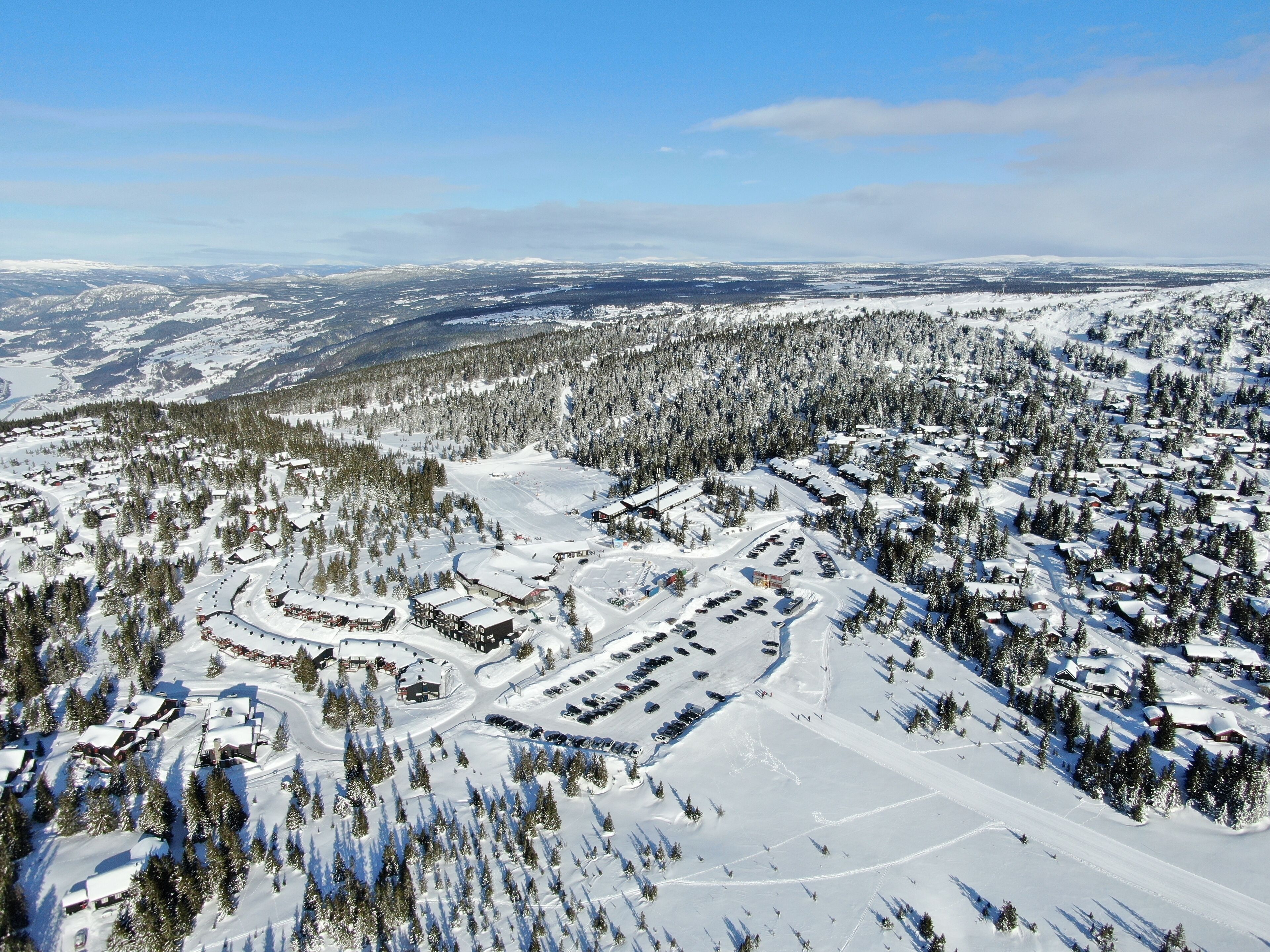 An aerial view of a snow-covered ski resort with multiple buildings, parking areas, and ski trails.