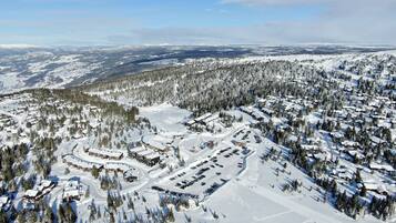 An aerial view of a snow-covered ski resort with multiple buildings, parking areas, and ski trails.