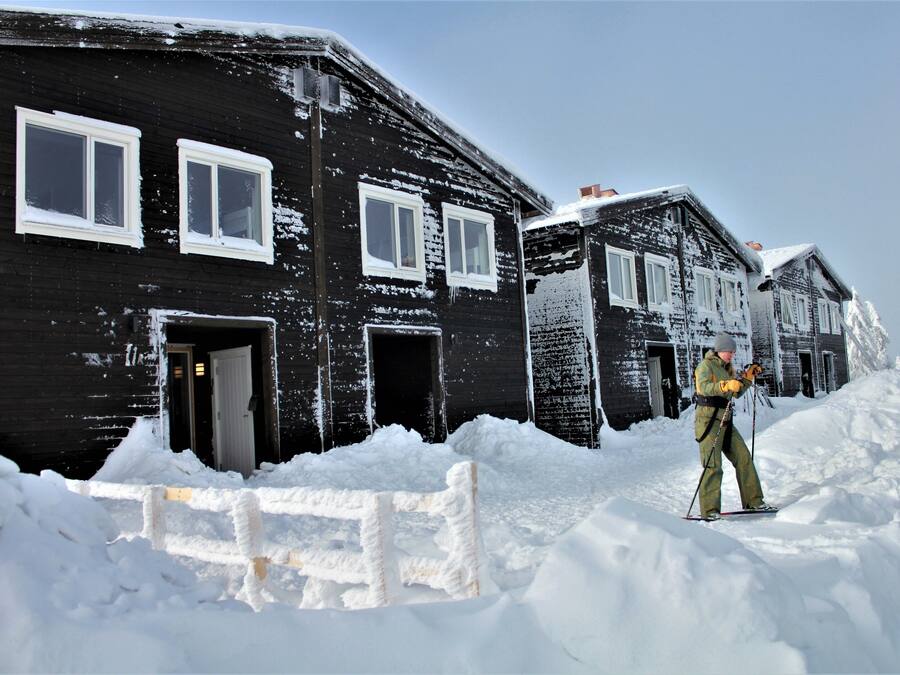A black wooden building with white-framed windows and a person skiing in the snow.