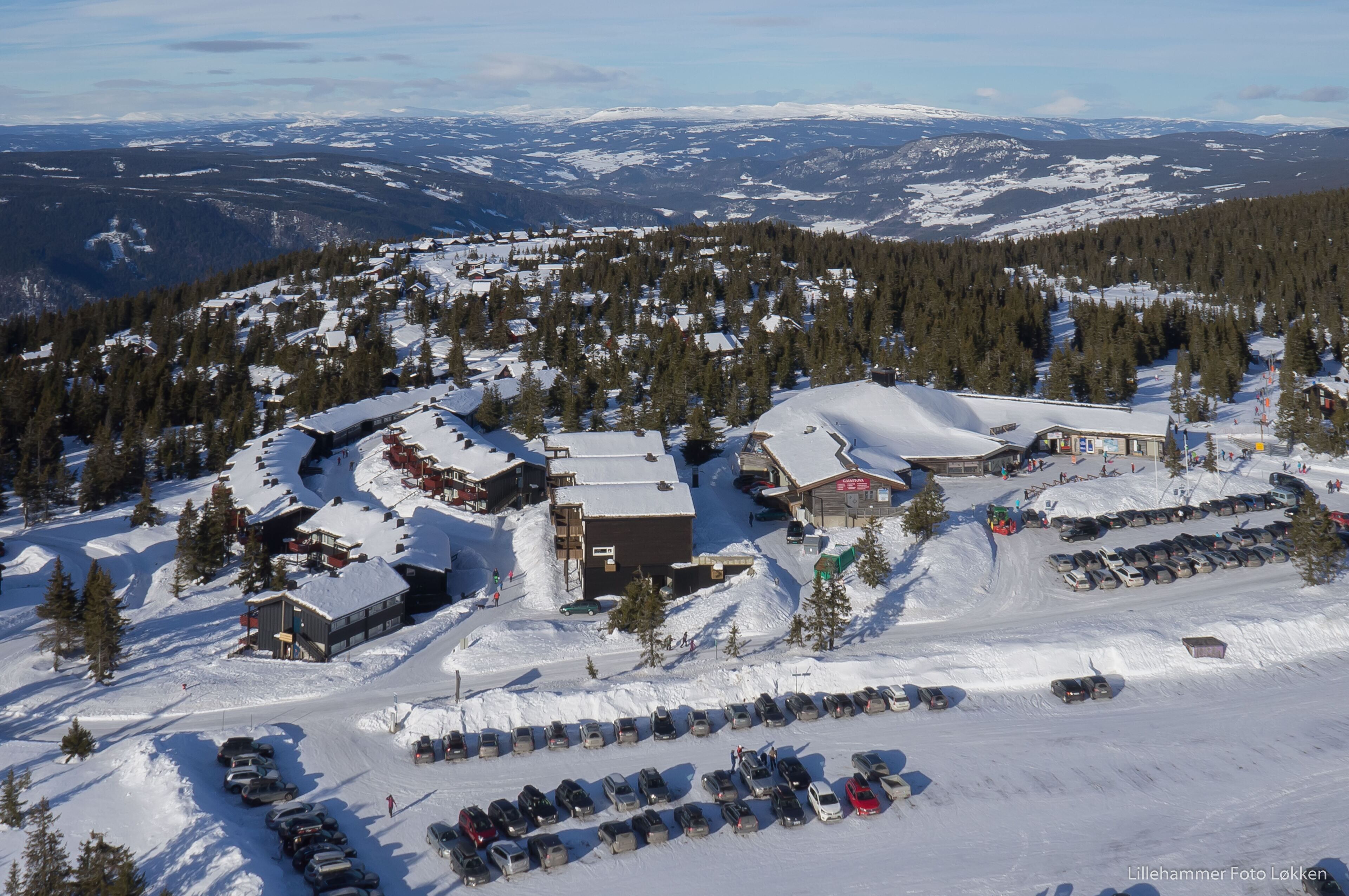 Estación de esquí nevada con varios edificios, zonas de estacionamiento y un telón de fondo montañoso.
