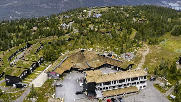 An aerial view of a mountain resort with buildings covered in grass roofs, surrounded by dense forests and a winding road. - Hafjell Resort Hafjelltoppen Gaiastova (Øyer)