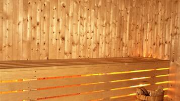 A wooden sauna bench with a glass bucket on the floor.