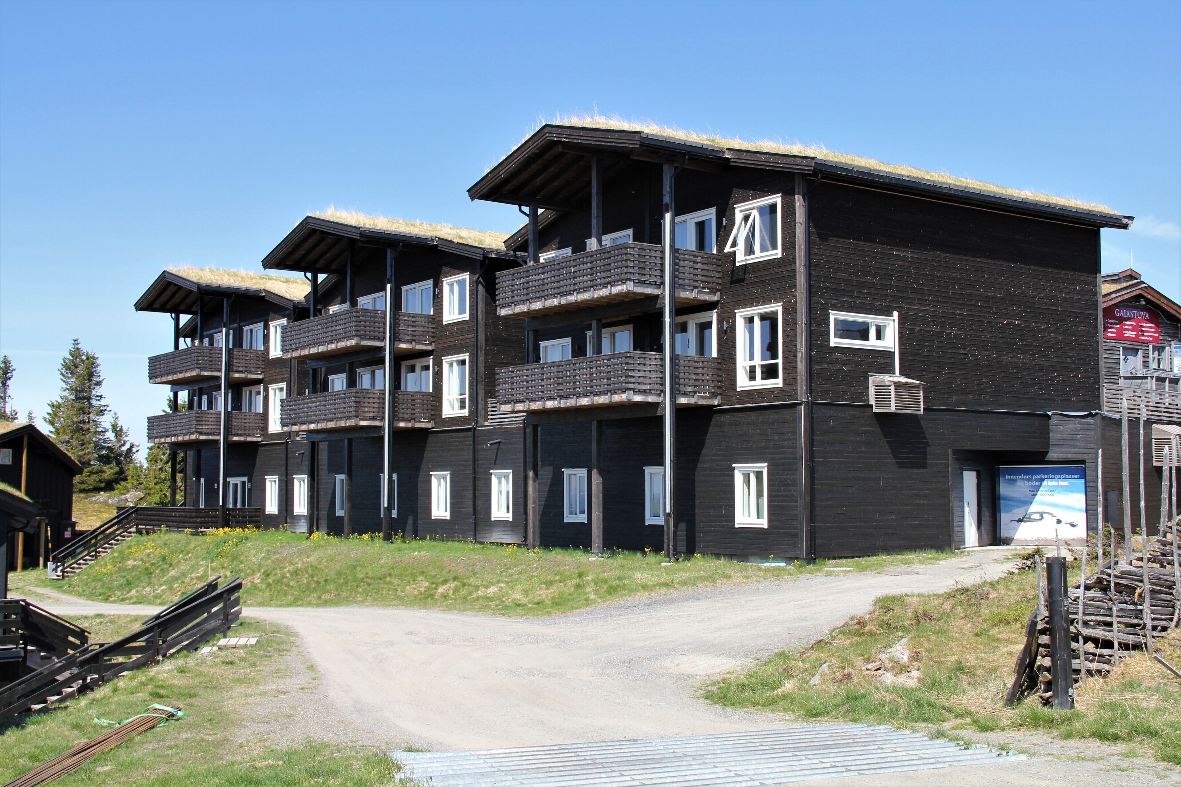 A multi-story building with balconies, a dirt path leading to the entrance, and a signboard.