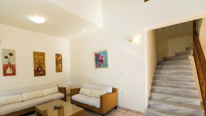 A living room with a sofa, armchair, and coffee table, a staircase, and wall art.