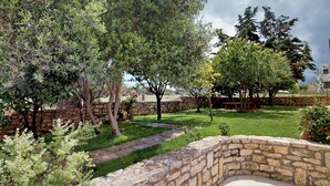 A stone-walled garden with a grassy lawn, trees, and a stone bench.