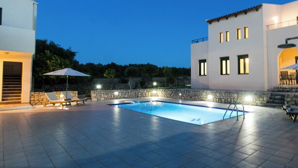 A swimming pool with a stone wall and a white building with multiple windows.