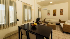 A dining area with a table, chairs, and a fruit bowl. There is a sofa and a television in the background.